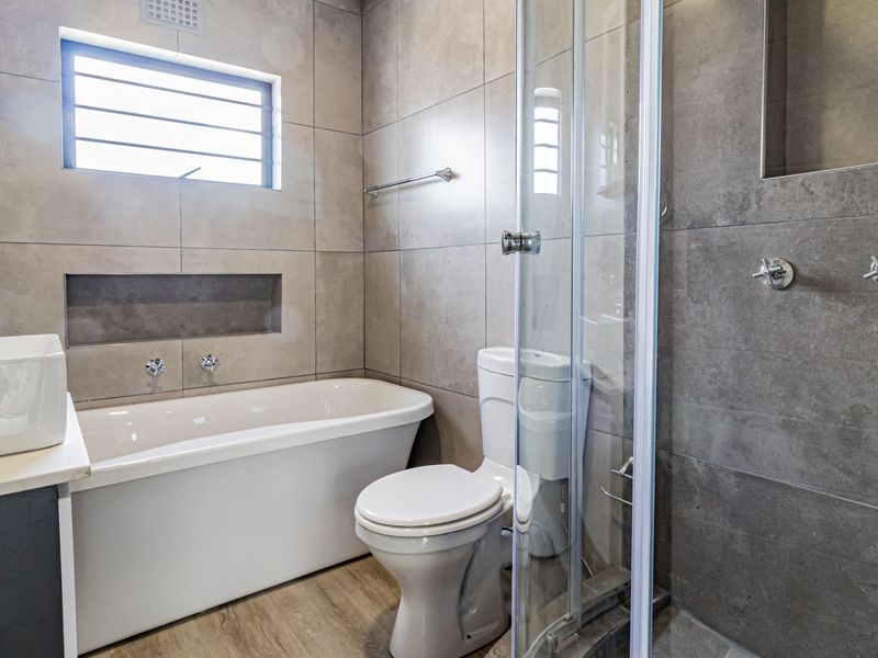 Modern bathroom featuring a freestanding bathtub, glass-enclosed shower, vessel sink vanity, and neutral floor-to-ceiling tiling with a convenient recessed wall niche.