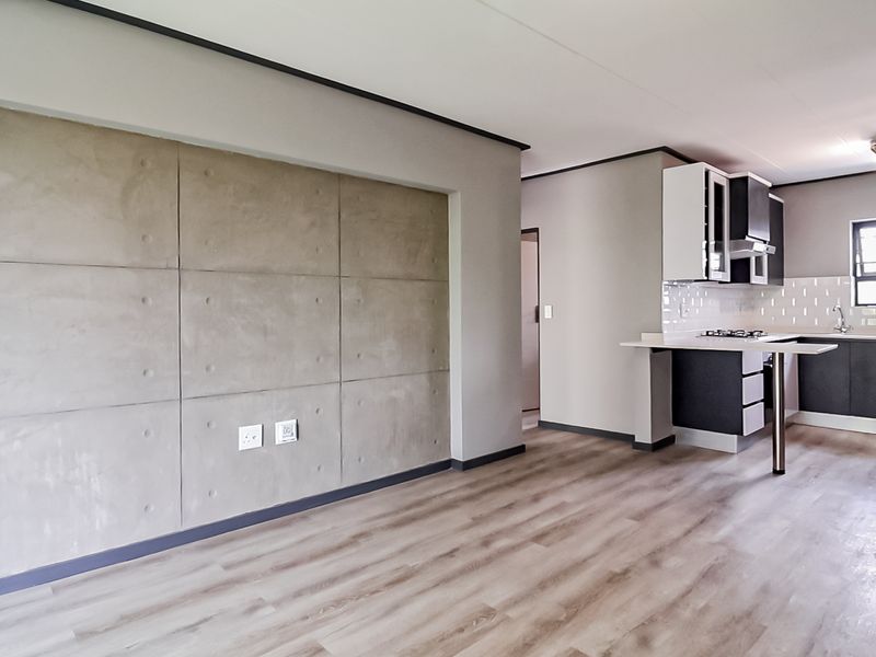 Modern open-plan living area featuring laminate flooring, a concrete feature wall, and a contemporary kitchen with built-in cabinetry and a breakfast bar.