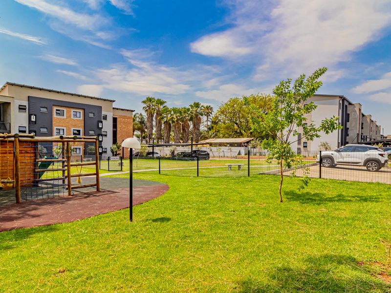 Communal outdoor area featuring a playground, landscaped garden, and paved parking access within a modern townhouse complex.