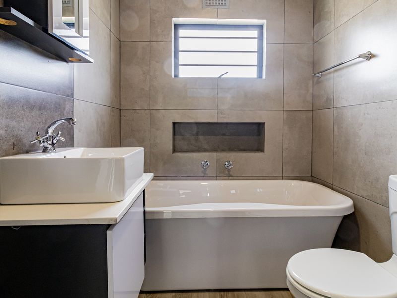 Modern bathroom featuring a freestanding bathtub, vessel sink on a vanity cabinet, recessed wall niche, and a glass-enclosed shower area with neutral tiling.