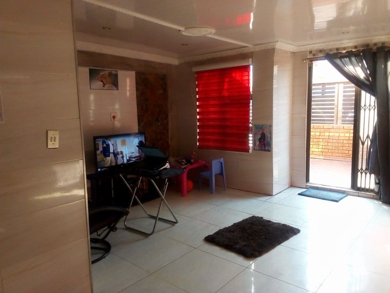 A living room featuring tiled walls and flooring, recessed ceiling lights, and a sliding door leading to an outdoor area with a security gate.