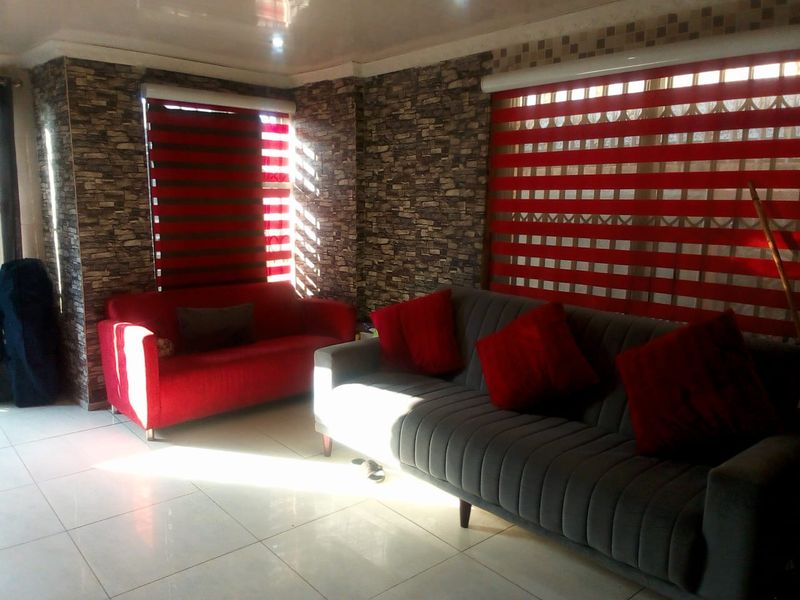 A living room featuring tiled flooring, faux stone wall cladding, and modern striped roller blinds.