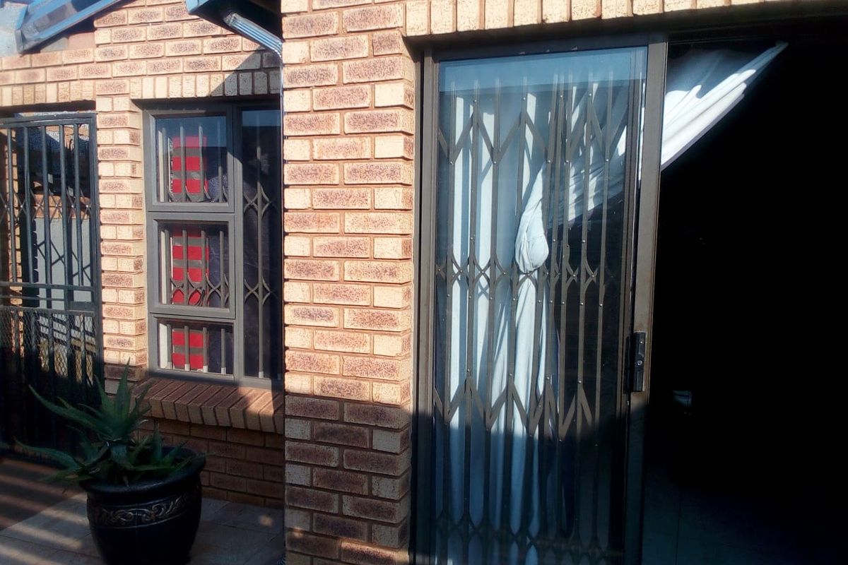 A view of the rear exterior featuring face brick walls, a sliding door with a security gate, and security bars on the window.
