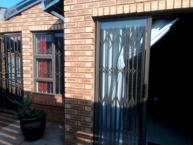 A view of the rear exterior featuring face brick walls, a sliding door with a security gate, and security bars on the window.
