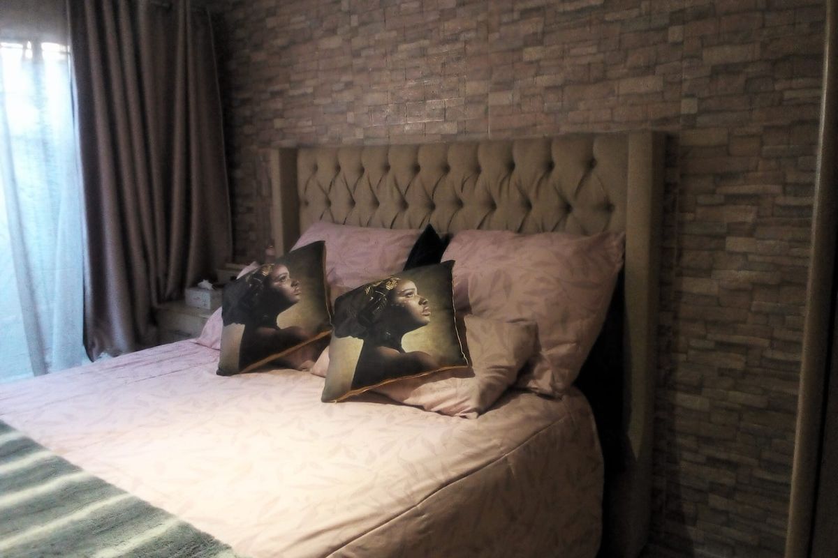 A bedroom featuring a textured brick-effect accent wall and a large upholstered headboard, creating a cozy and defined sleeping space.
