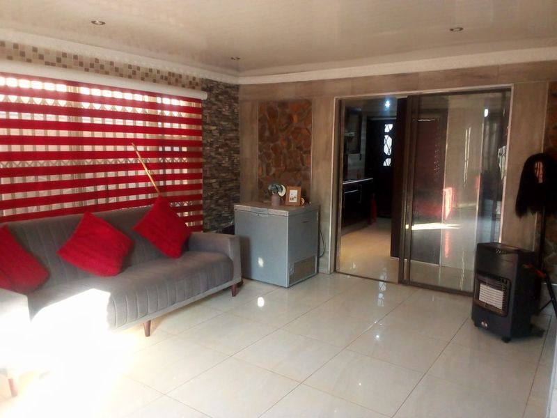 A living room featuring tiled flooring, a stone accent wall, and recessed ceiling lighting, with a sliding glass door leading to an adjacent space.
