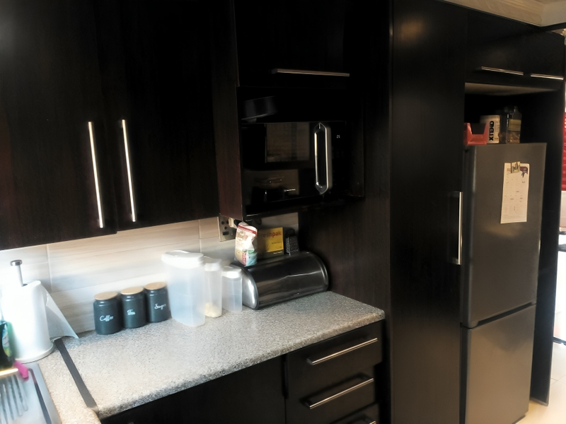 A modern kitchen area featuring dark wood cabinetry, granite countertops, and a built-in microwave unit with integrated fridge housing.