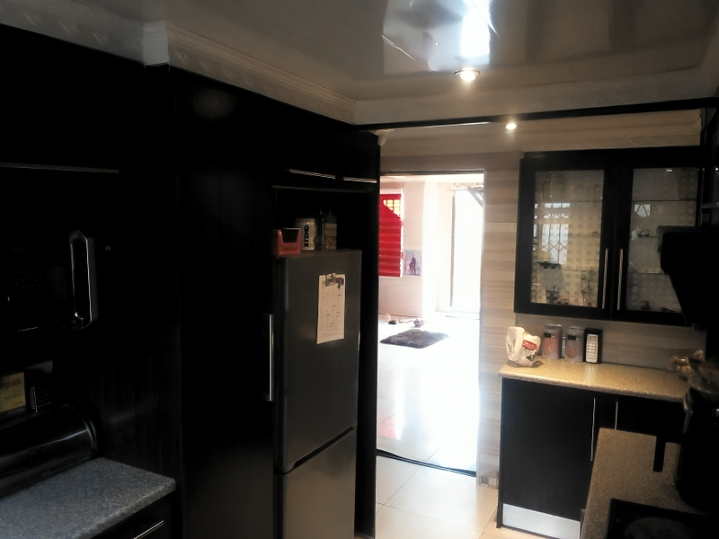 A functional kitchen featuring dark cabinetry, light-toned countertops, and glass-fronted display units, with a view leading into an adjacent living area.