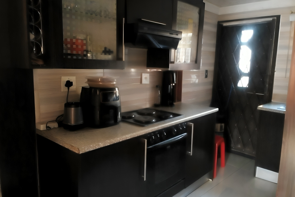 A compact kitchen featuring dark cabinetry, a built-in oven with electric hob, extractor fan, and tiled backsplash, leading to an exterior door.