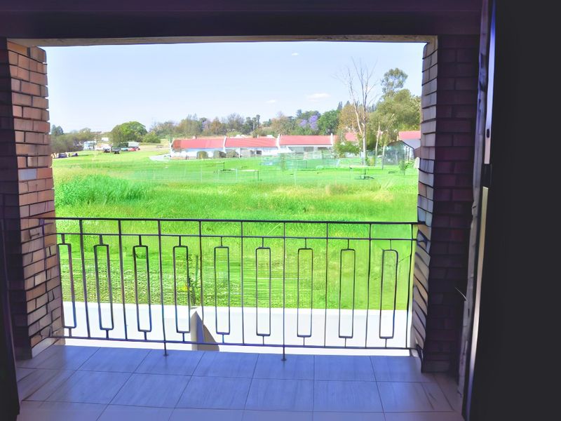 A covered balcony featuring tiled flooring, exposed brick pillars, and a metal balustrade, offering an open view of the surrounding green landscape.