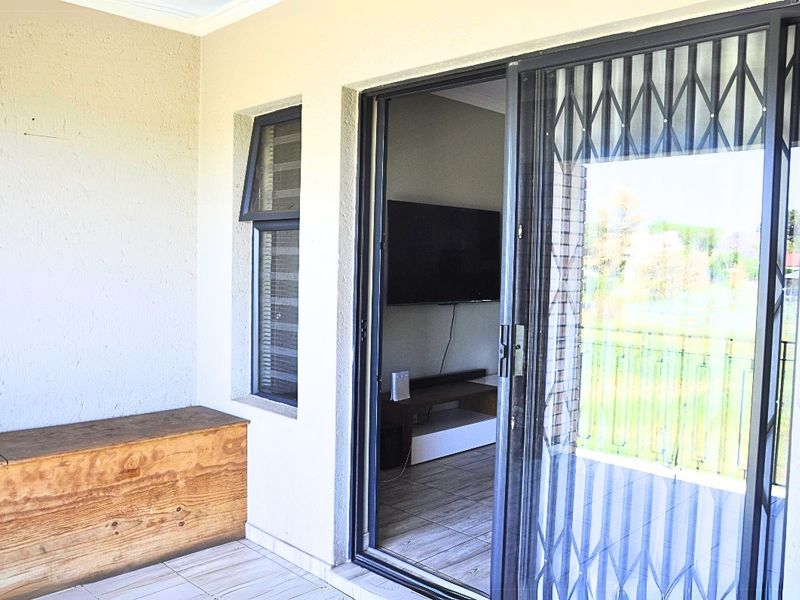 A covered balcony area featuring tiled flooring, a sliding glass door with a security gate, and a small casement window.