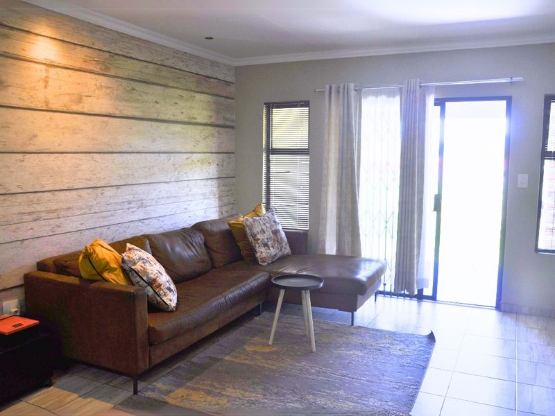 A well-lit living room featuring tiled flooring, a decorative wood-look feature wall, and a sliding glass door providing access to the exterior.