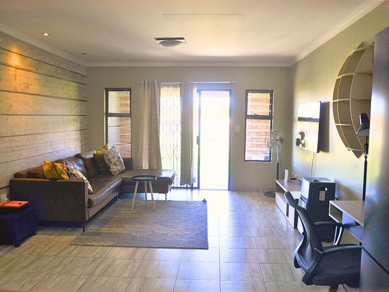 A well-lit living room featuring tiled flooring, a decorative feature wall, and direct access to an outdoor area through a sliding security door.