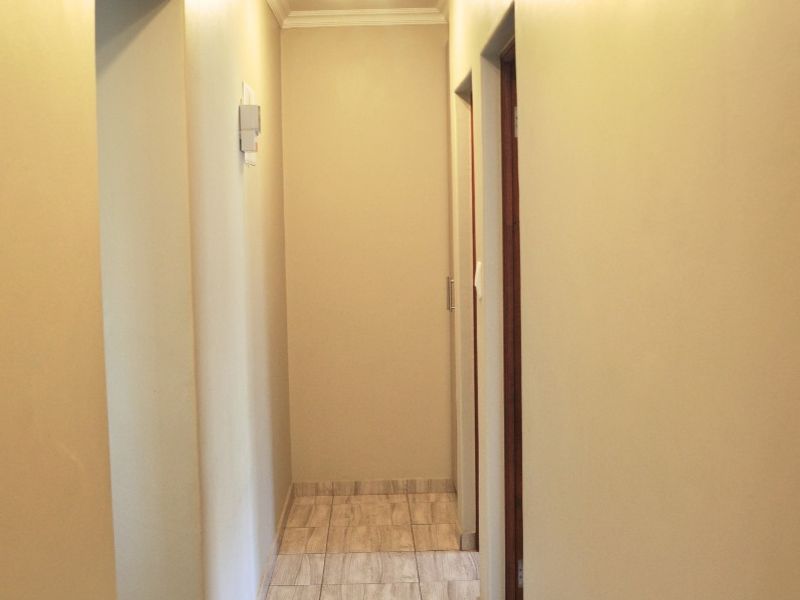 A clean, empty hallway featuring neutral wall tones, wood-look tiled flooring, and a simple ceiling light fixture.