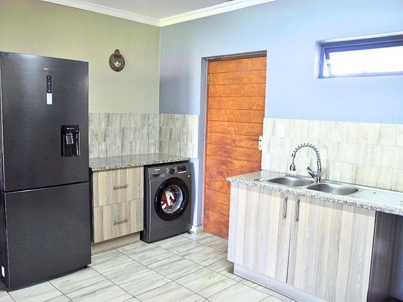 A functional kitchen featuring granite countertops, double stainless steel sink, laminate cabinetry, and tiled flooring with a neutral color palette.