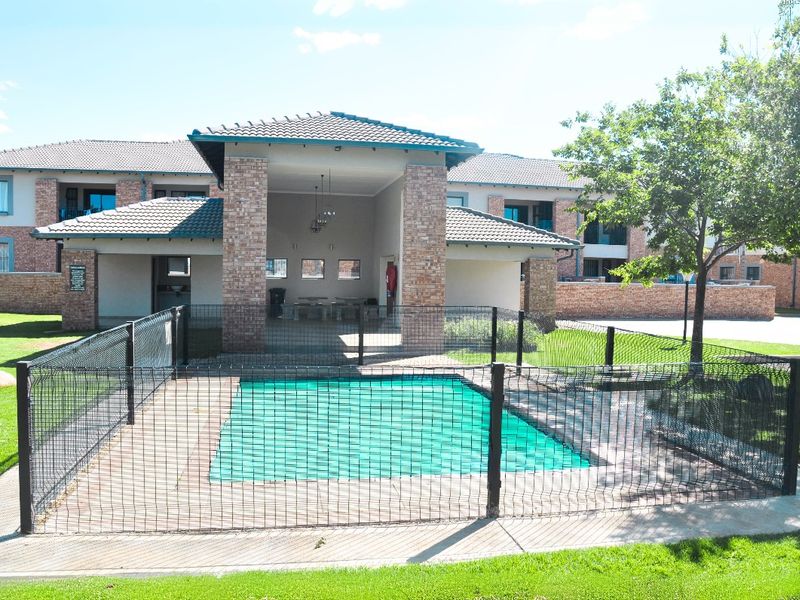Communal swimming pool area featuring a safety net, paved surround, and a covered patio structure with brick pillars within an apartment complex.