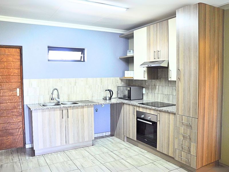 Modern kitchen featuring wood-grain cabinetry, granite countertops, integrated oven and hob, and tiled flooring with a neutral backsplash.