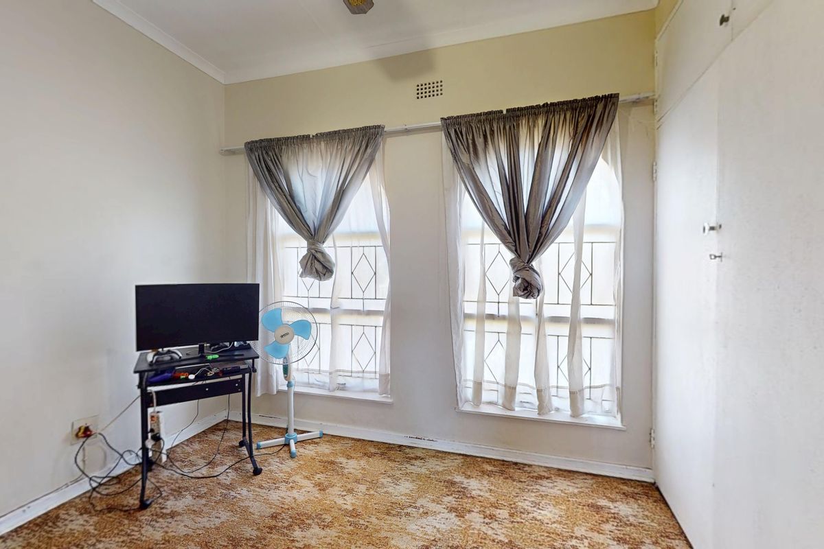 A bedroom featuring built-in wardrobe storage, security bars on the windows, and carpet flooring, offering a blank canvas for renovation.