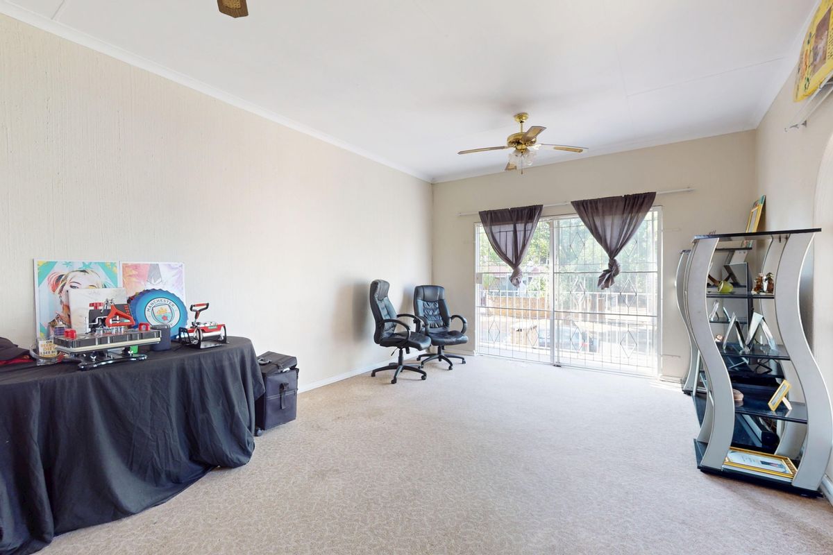 Spacious living room featuring neutral walls, carpet flooring, a ceiling fan, and an arched window with access to a sliding glass door.