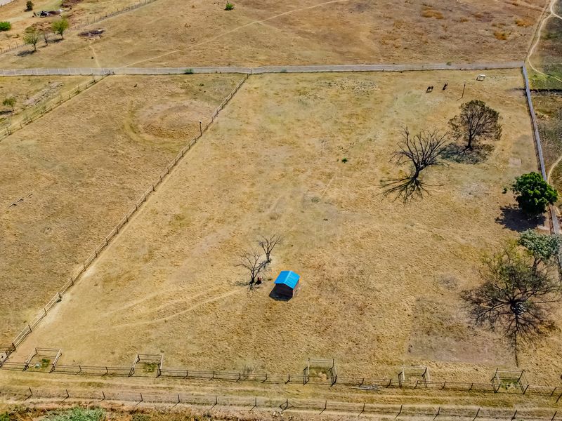Aerial view of a large, open residential vacant land plot featuring perimeter fencing, scattered mature trees, and a small storage shed.