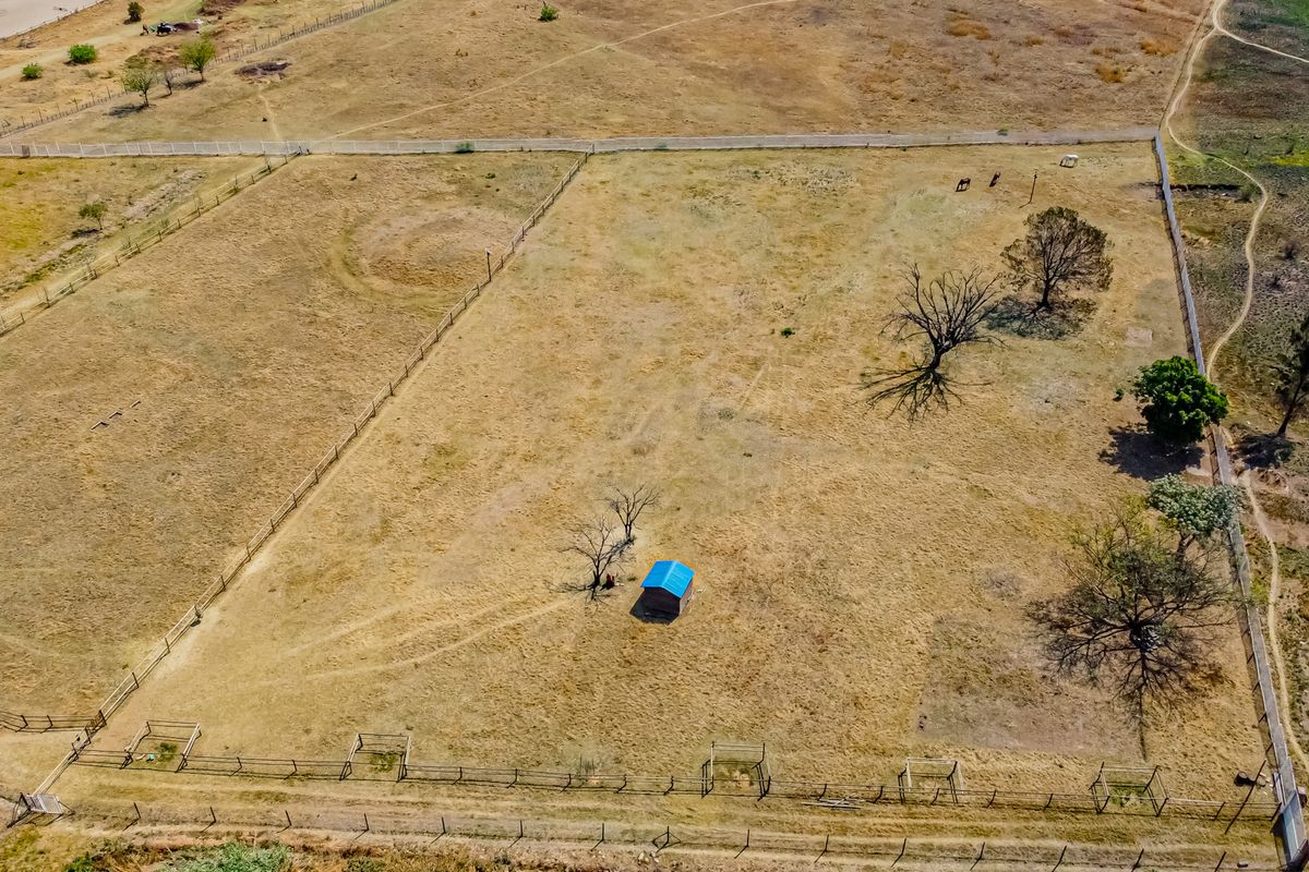 Aerial view of a large, open residential vacant land plot featuring perimeter fencing, scattered mature trees, and a small storage shed.