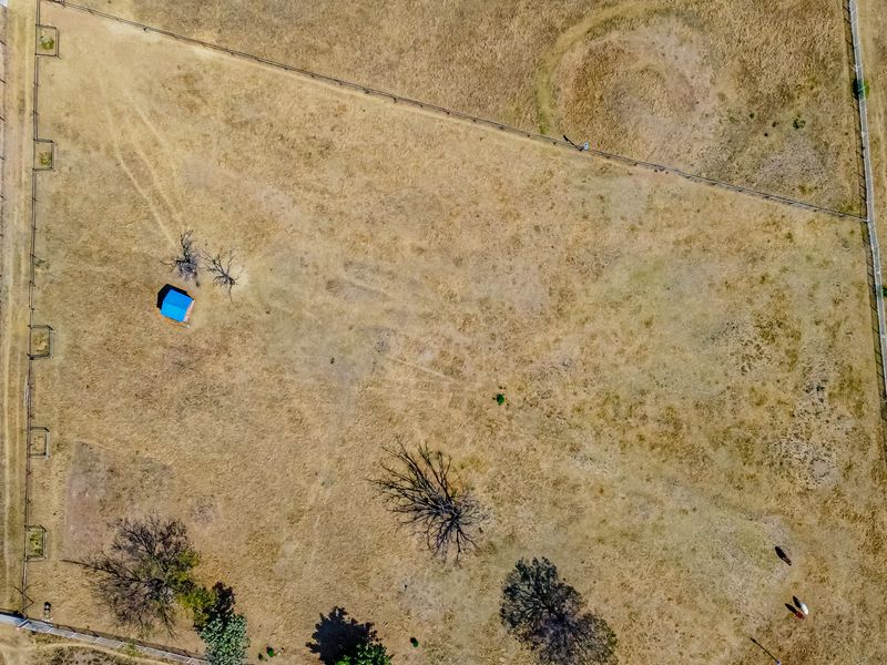 Aerial view of a large, dry residential vacant land plot featuring perimeter fencing, a small shed, and scattered mature trees.