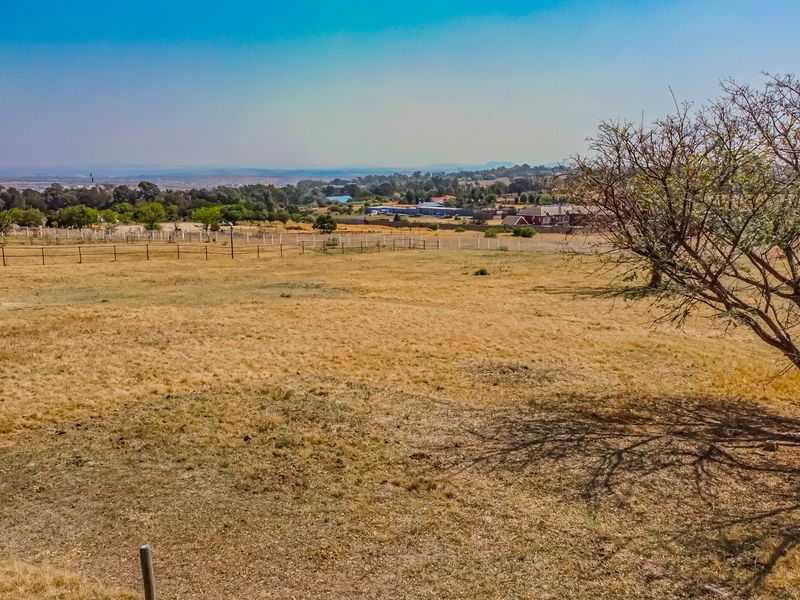 A wide-angle view of the vacant residential land, featuring dry grass, mature trees, perimeter fencing, and a small storage shed.