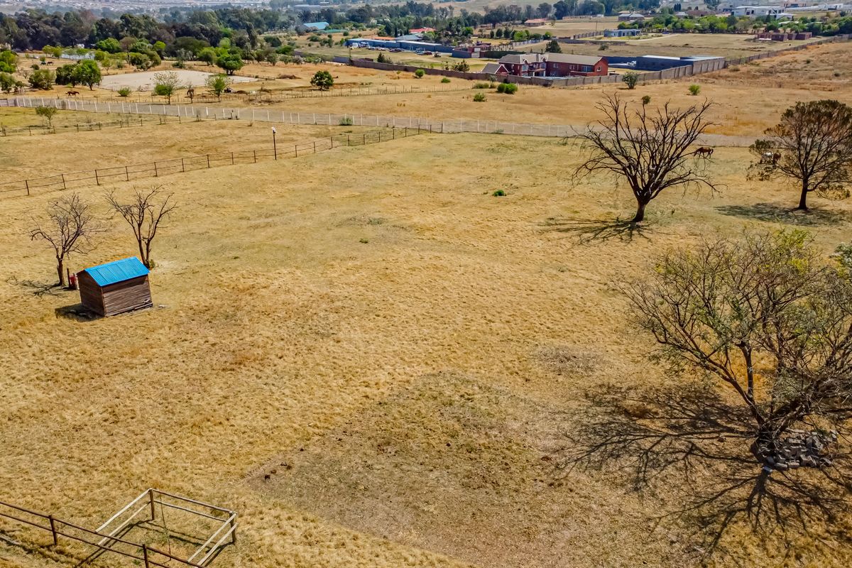 An aerial view of a large, open residential vacant land plot featuring perimeter fencing, mature trees, and a small storage shed.