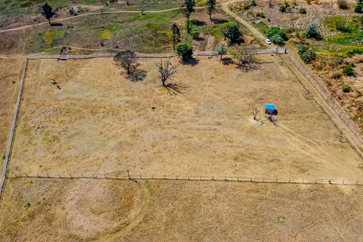 Aerial view of a large, open residential vacant land plot featuring perimeter fencing and a small shed structure.
