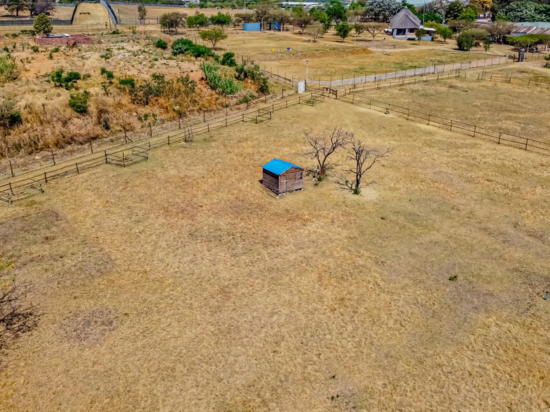 An aerial view of a large, open residential vacant land plot featuring perimeter wire fencing and a small wooden storage shed.