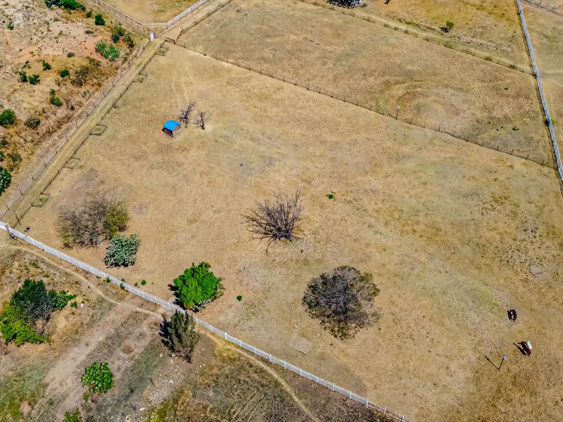 Aerial view of a large, fenced vacant residential plot featuring dry grass, scattered trees, and a small storage shed.
