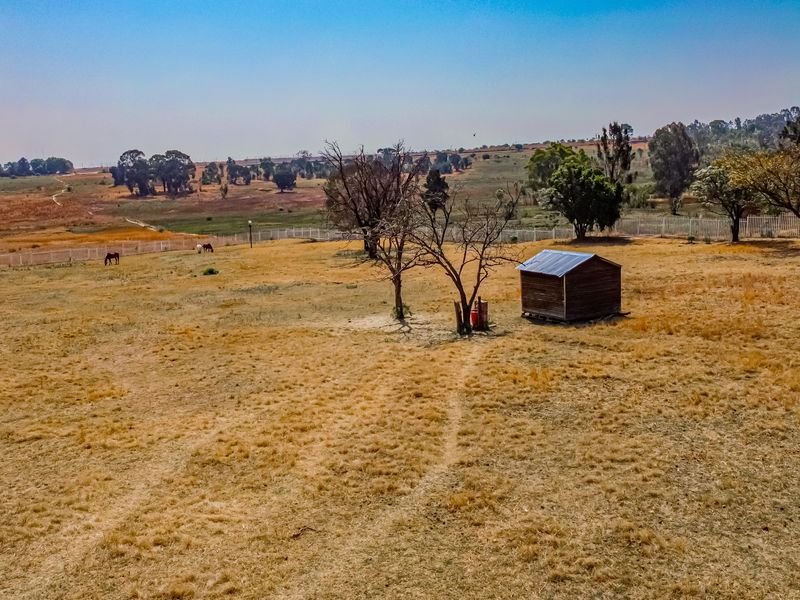 An aerial view of a large, open residential vacant land plot featuring dry grass, perimeter fencing, and a small wooden storage shed.
