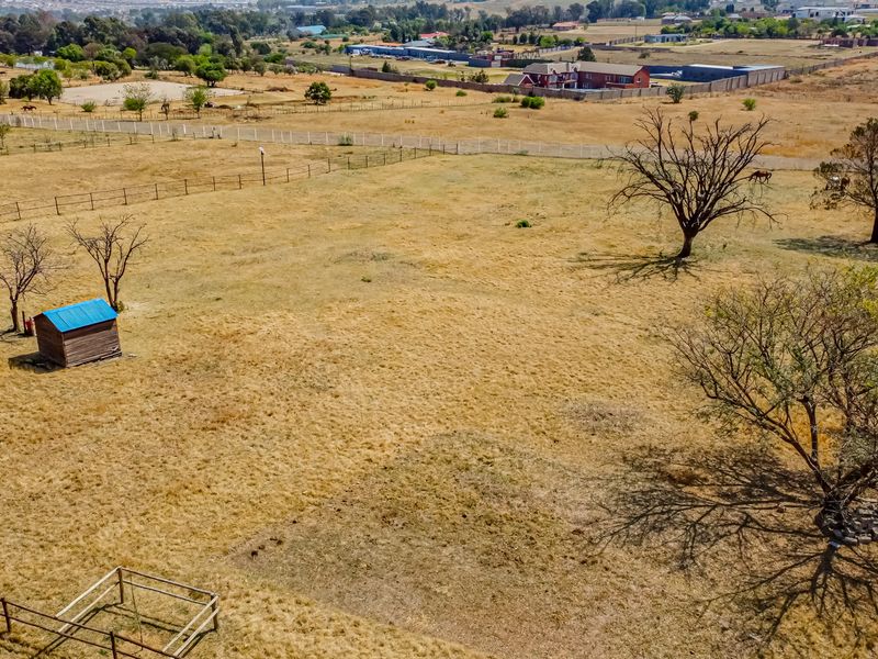 An aerial view of a large, open residential vacant land plot featuring perimeter fencing, mature trees, and a small storage shed.