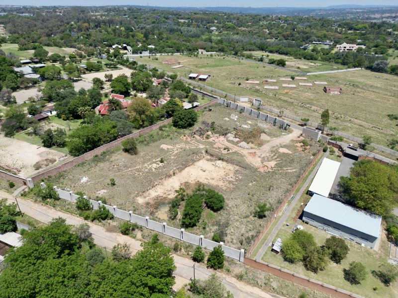Aerial view of a vacant residential plot featuring perimeter walling and established boundary fencing in a semi-rural setting.