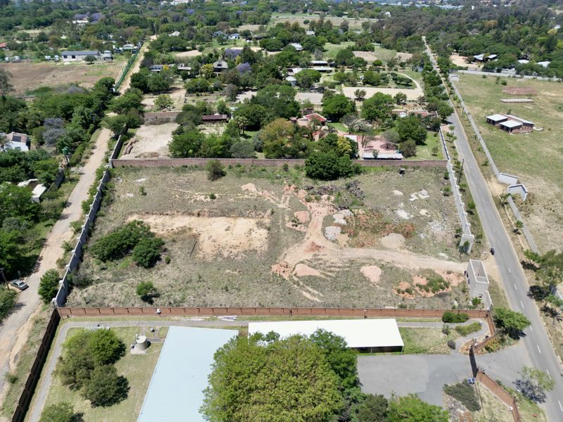 Aerial view of a large, vacant residential plot enclosed by perimeter brick walls, featuring some existing paved areas and a small metal roof structure.