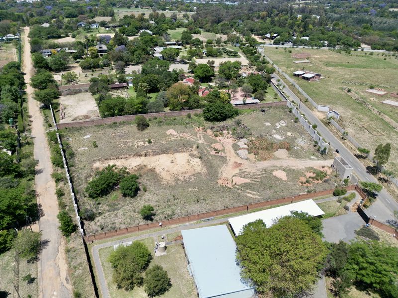Aerial view of a vacant residential plot featuring perimeter walling and direct access to a paved road in a developed neighborhood.