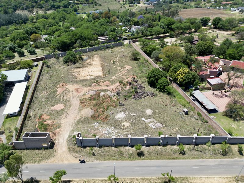 Aerial view of a vacant residential plot featuring perimeter walling and a gated entrance structure, situated in a developed neighborhood.