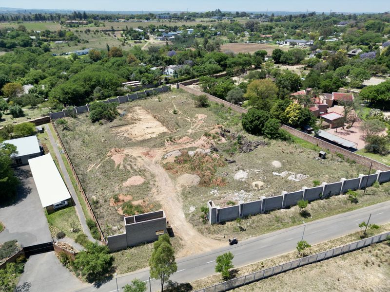 Aerial view of a vacant residential plot featuring perimeter walling, a paved driveway, and an existing carport structure in a suburban setting.