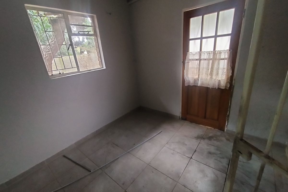 An empty bedroom featuring tiled flooring, a timber-framed door with glass panes, and a window with security bars.