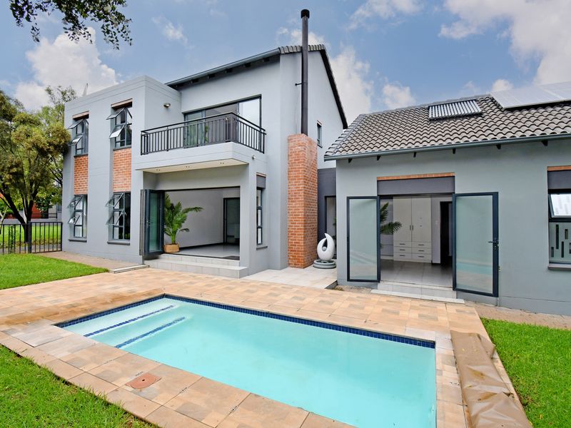 Rear view of a modern two-story house featuring a swimming pool, tiled patio area, balcony, and solar panels on the roof.