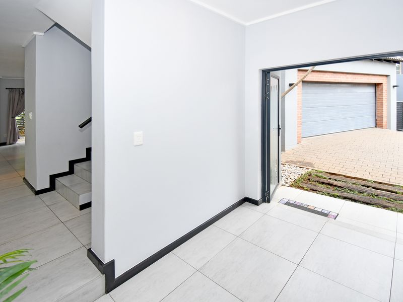 Bright and modern entrance hall featuring neutral tiled flooring, a clean staircase with a handrail, and direct access to the exterior driveway area.
