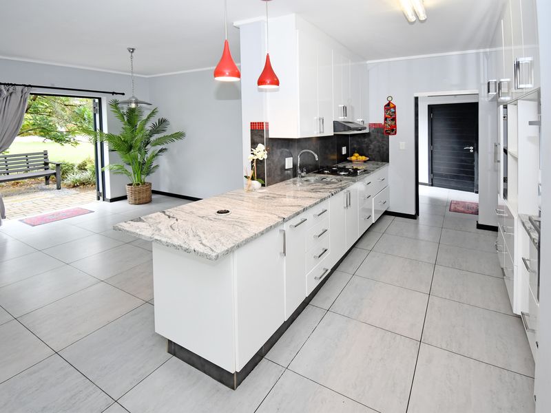 Modern open-plan kitchen featuring granite countertops, white cabinetry, and tiled flooring, with seamless access to the outdoor patio area.