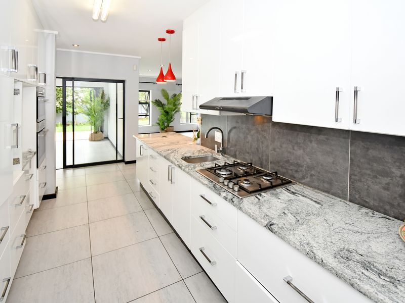 Modern kitchen featuring white cabinetry, granite countertops, gas hob, extractor fan, and tiled flooring, with direct access to an outdoor patio area.