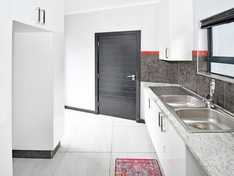 A clean, modern kitchen featuring white gloss cabinetry, granite countertops, a double stainless steel sink, and neutral tiled flooring.