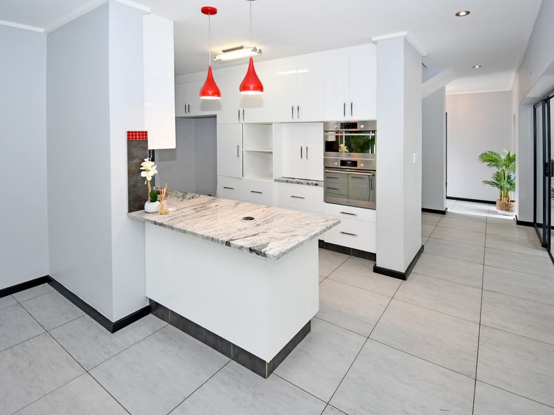 Modern kitchen featuring gloss white cabinetry, granite countertops, built-in oven and microwave, and neutral tiled flooring in an open-plan layout.