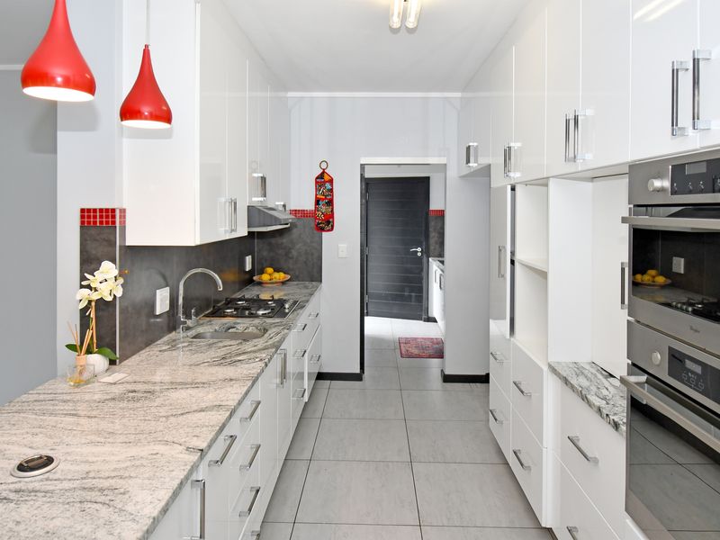 Modern galley-style kitchen featuring high-gloss white cabinetry, granite countertops, integrated stainless steel appliances, and tiled flooring.