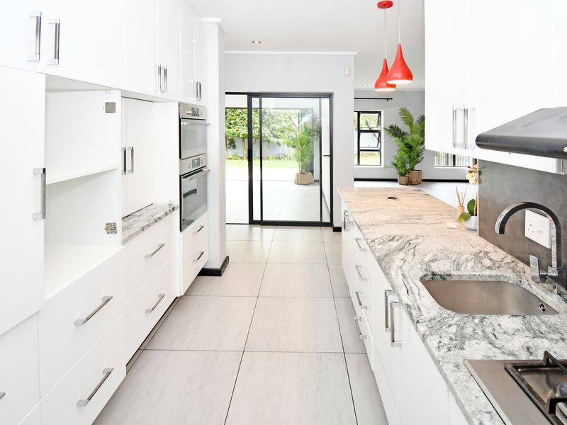 Modern kitchen featuring white cabinetry, granite countertops, built-in appliances, and tiled flooring, with direct access to the outdoor patio area.