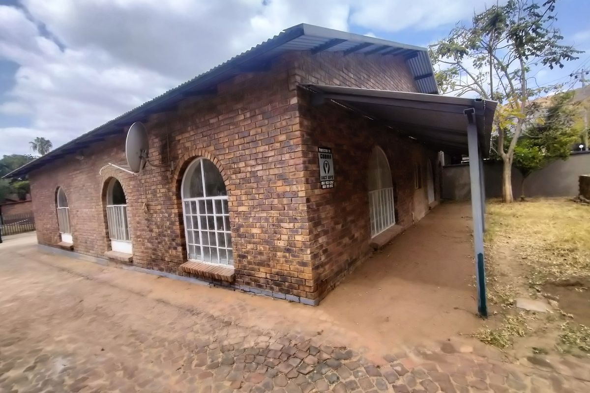 Rear view of a face brick house featuring arched windows, a corrugated metal roof, and a covered patio area overlooking the garden.