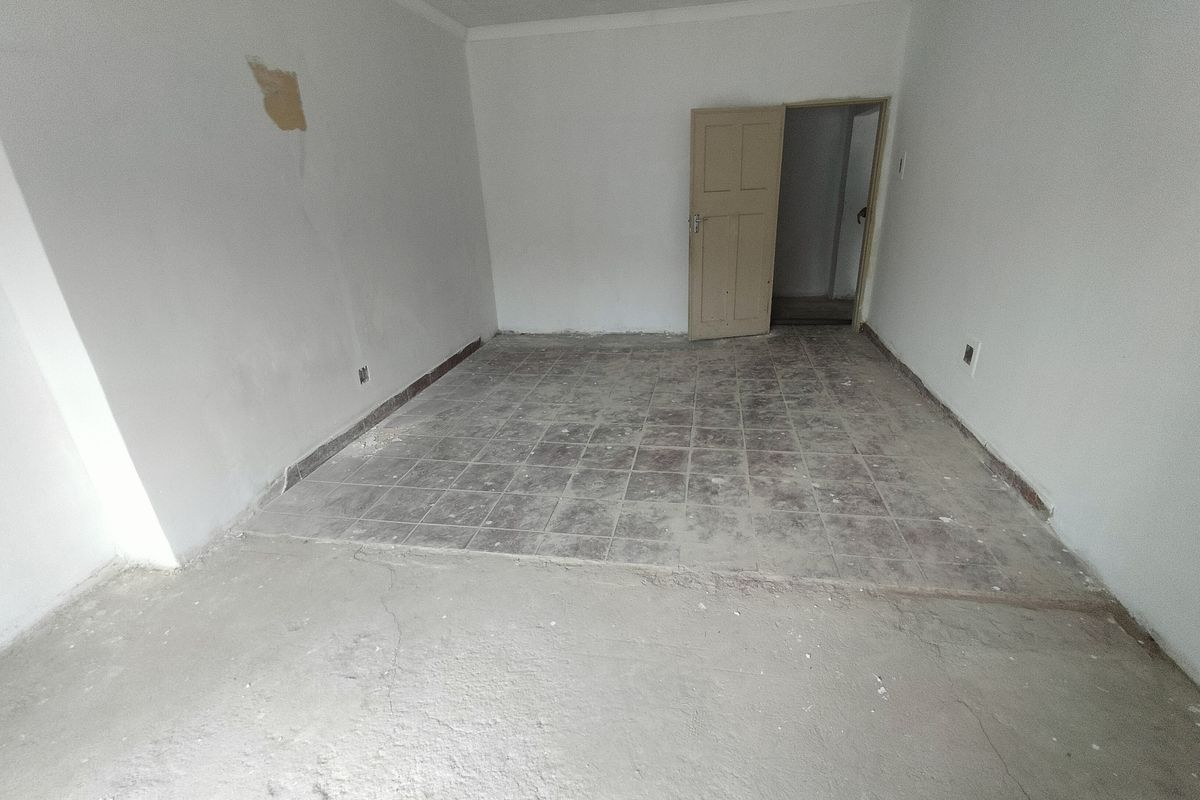 An empty, unfinished living area featuring a mix of concrete and tiled flooring, requiring cosmetic renovation and wall repairs.