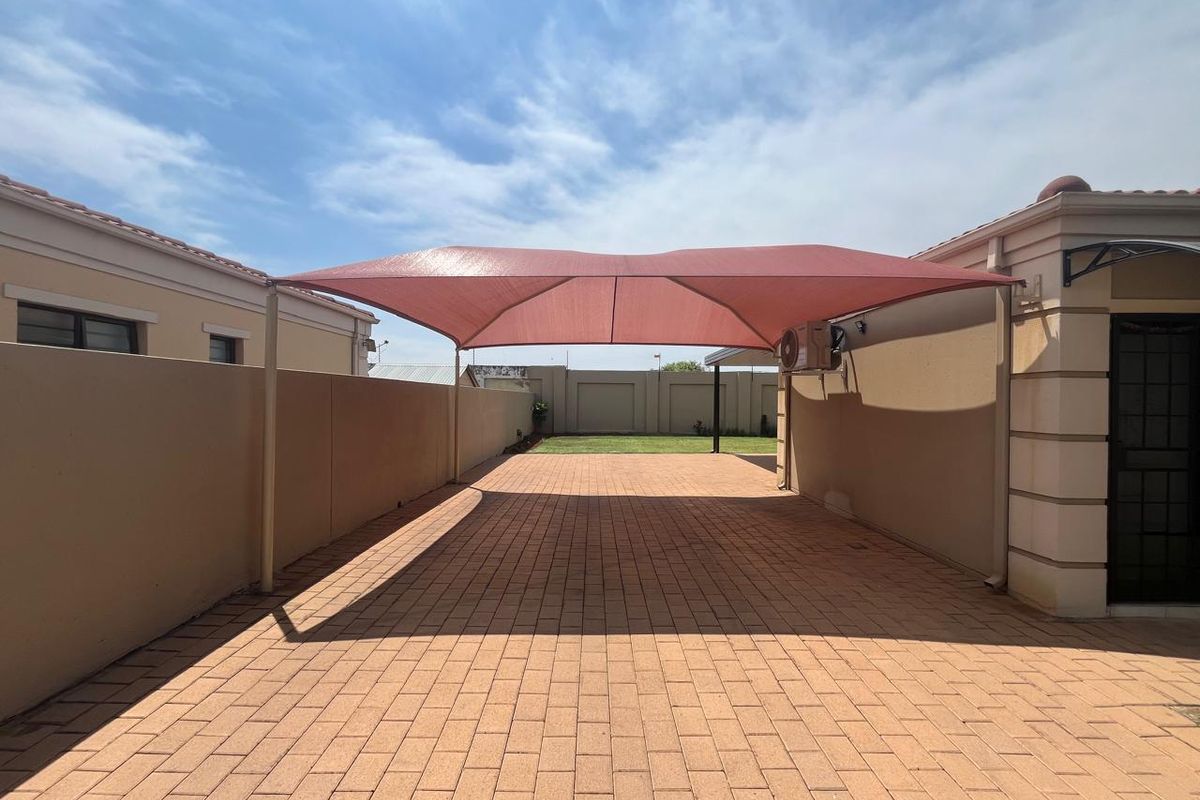A paved rear courtyard area featuring a large shade sail structure, perimeter boundary walls, and an external air conditioning unit.